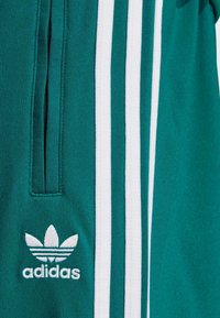 Morske adidas trenirke s bijelim tri pruge, patentnim zatvaračem na džepu i bijelim adidas trefoil logom izvezenim ispod džepa.