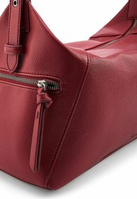 Bolso de hombro de cuero rojo con un acabado texturizado, que cuenta con un bolsillo con cremallera y un detalle de cuero anudado en el tirador de la cremallera.