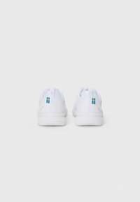Las zapatillas deportivas blancas presentan una parte superior de malla, una suela blanca texturizada y un acento azul y amarillo en el talón. Diseño minimalista con tiradores.
