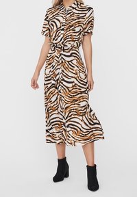 Sukienka zapinana na guziki z wzorem w paski tygrysa w kolorze czarnym, pomarańczowym i białym. Materiał jest lekki; sukienka ma pasek w talii i krótkie rękawy.