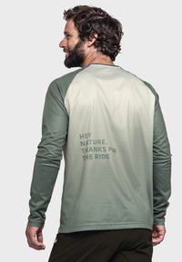 Langärmliges, grünes Sportshirt aus strukturiertem Material mit einem Farbverlauf von hellgrün nach dunkelgrün und Text auf dem Rücken: "HEY NATUR, DANKE FÜR DIE FAHRT."