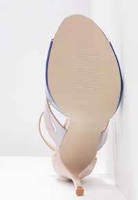 Sandale à talon haut avec semelle beige, brides supérieures rose clair et bleues, vue par la semelle sur fond blanc.
