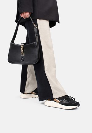 Sac à main noir avec quincaillerie dorée, associé à un pantalon large noir et beige et des baskets noires avec un design texturé.