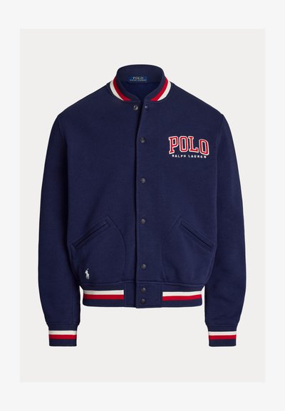 Temno modra varsity jakna z gumbi, z rdeče-belimi črtastimi ovratnikom, manšetami in robom; logotip »POLO Ralph Lauren« na prsih in oznaka Pony na žepu.