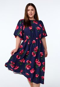 Bloemenjurk in donkerblauwe stof, met grote roze rozen en groene bladeren. Losse pasvorm met een geraffineerde taille en korte, brede mouwen.