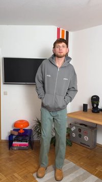 Sudadera gris con cremallera y gran bolsillo, combinada con pantalones rectos de color verde claro y botas color marrón claro. Diseño sencillo, corte relajado y textura suave.