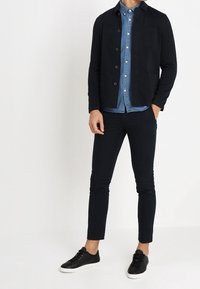 Ciemnoniebieska, casualowa kurtka z guzikami na jasno-niebieskiej koszuli dżinsowej. Slim-fit czarne spodnie i czarne trampki z białymi podeszwami.