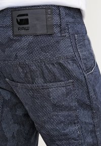 Jeans de mezclilla de un azul oscuro con un patrón texturizado, parche de cuero con el logo de G-Star RAW y detalles en los bolsillos laterales.