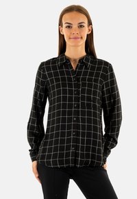 Camisa negra de botones con patrón de cuadrícula blanca, mangas largas, bolsillo en el pecho y textura suave, con un corte recto y cuello.
