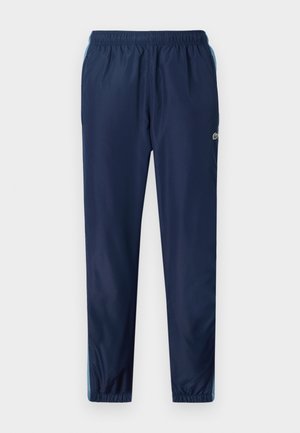 Pantaloni sportivi blu navy con vita elasticizzata, gambe affusolate e accenti azzurri lungo i lati; realizzati in un materiale leggero e liscio.