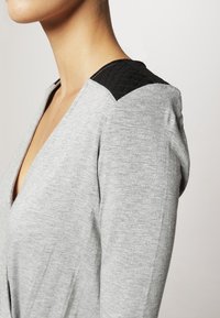 Haut gris en V avec un détail d'épaule matelassé noir texturé, fabriqué en tissu doux et à coupe décontractée, avec des coutures visibles.