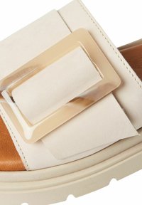 Sandale à glissière beige avec un upper en cuir texturé, dotée d'une grande boucle en plastique translucide et d'un semelle intérieure en mousse de couleur marron clair.