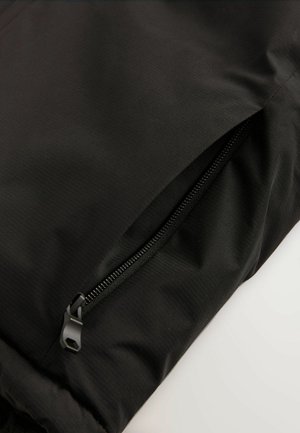 Schwarze Jacke mit einer Reißverschlusstasche. Der Stoff hat eine glatte Textur mit einem subtilen Glanz, und der Reißverschluss hat eine kontrastierende Farbe.