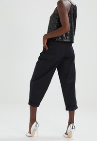 Débardeur noir à sequins avec une coupe carrée, associé à un pantalon court bleu marine. Talons hauts argentés complètent la tenue. Textures lisses et accents brillants.