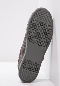 Grau gummierter Schuhsohle mit einem strukturierten Muster, das einen glatten zentralen Bereich und einen rechteckigen Akzent mit Größenmarkierung aufweist.
