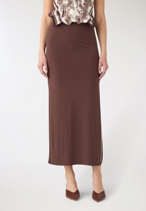 Donna che indossa una gonna lunga marrone a vita alta, taglio dritto con spacco laterale, abbinata a tacchi marroni a punta e top stampato.
