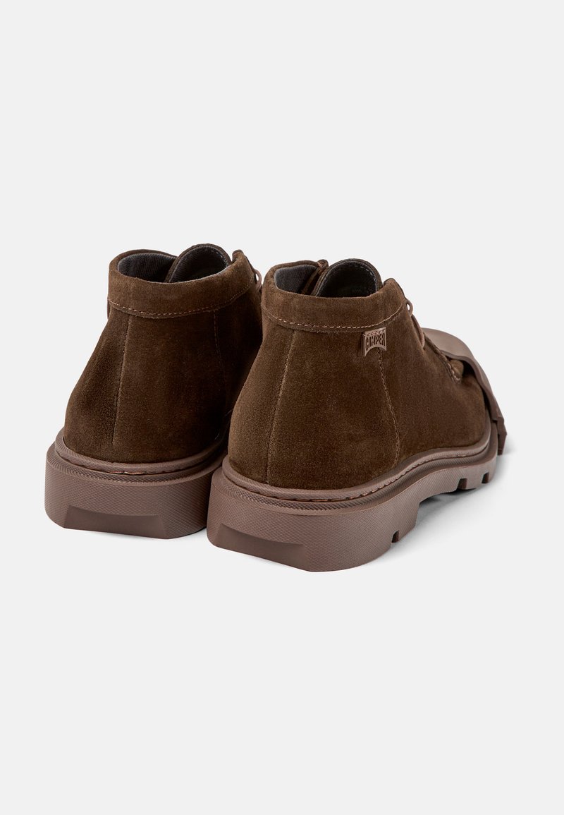 Bottines en suede marron avec une semelle en caoutchouc épaisse, de forme arrondie et un design minimaliste. Comprend des coutures discrètes et un détail d'étiquette.