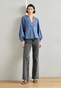 Denimbluse i lyseblå med V-hals og ballongerm. Kombinert med høyt liv grå brede bukser og svarte sandaler med stropper.