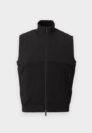 Chaleco negro sin mangas con cuello alto, cremallera frontal, dos bolsillos con cremallera y una combinación de tela lisa y texturizada.