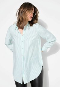 Camisa de botones de rayas azul claro y blanca con cuello, mangas largas y dobladillo curvo. Fabricada en una tela ligera.