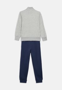 Sweat-shirt gris avec un col montant et des poignets côtelés, associé à un pantalon de jogging bleu marine avec des poignets élastiques. Les deux sont en tissu doux.