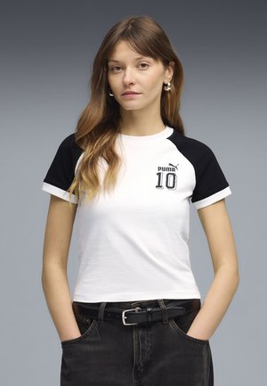 T-shirt blanc à manches courtes avec manches raglan noires, arborant un logo imprimé "Puma 10" sur le devant. Porté avec un jean noir taille haute.