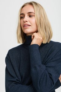 Dunkelblauer Rollkragenpullover mit gerippter Textur und langen Ärmeln, der eine lockere Passform und subtile Glitzerdetails im gesamten Stoff aufweist.