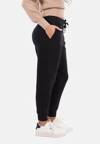 Pantaloni jogger neri con polsini elasticizzati, vita con coulisse e tasche laterali, abbinati a sneakers bianche con accenti neri.
