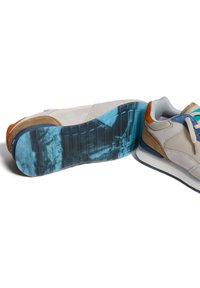 Sneakers con una parte superiore grigio chiaro, accenti in suede marrone e una suola blu traslucida con un motivo testurizzato. I lacci sono in colori pastello.