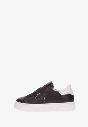 Zapatilla deportiva de cuero negro con suela y tacón de goma blancos, diseño con cordones y un logotipo de escudo en el panel lateral.