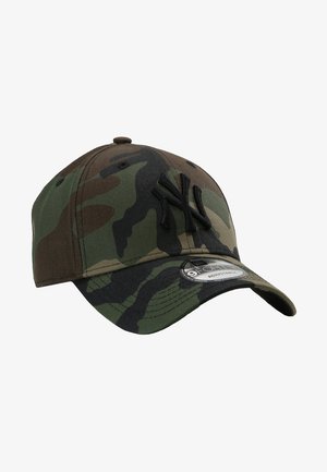 Kamuflasje baseballcap med brodert New York-logo i svart, laget av stoff med justerbar stropp, som viser forskjellige nyanser av grønt og brunt.