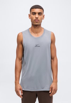 Jeune homme aux cheveux courts portant un haut de sport gris sans manches Nike Pro, debout devant un fond clair uni.