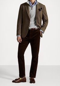 Blazer marron à chevrons, pull gris clair à col zippé, pantalon en velours côtelé marron foncé, mocassins marron avec glands et chaussettes à motifs.