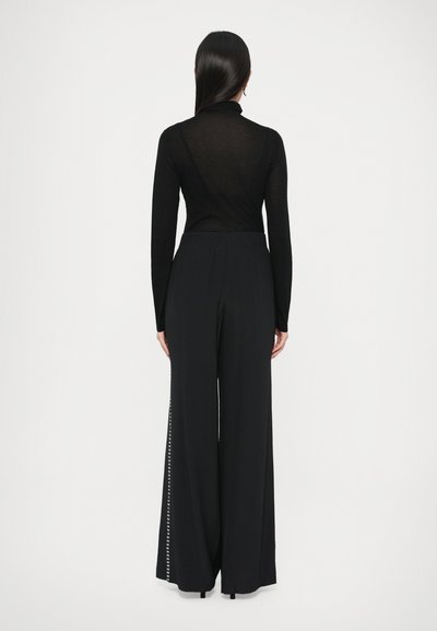 Czarny top z długim rękawem o dopasowanym kroju. W połączeniu z luźnymi, czarnymi, szerokimi spodniami z pionową linią małych ćwieków po boku.