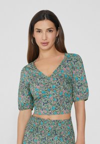 Zelený květinový cropped top s výstřihem do V, krátkými puff sleeves a složitými paisley vzory v modrofialových a růžových detailech.