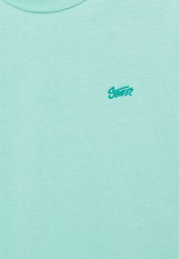 T-shirt turquoise clair à col rond avec petit logo "Snatz" brodé en bleu sarcelle sur la poitrine gauche.
