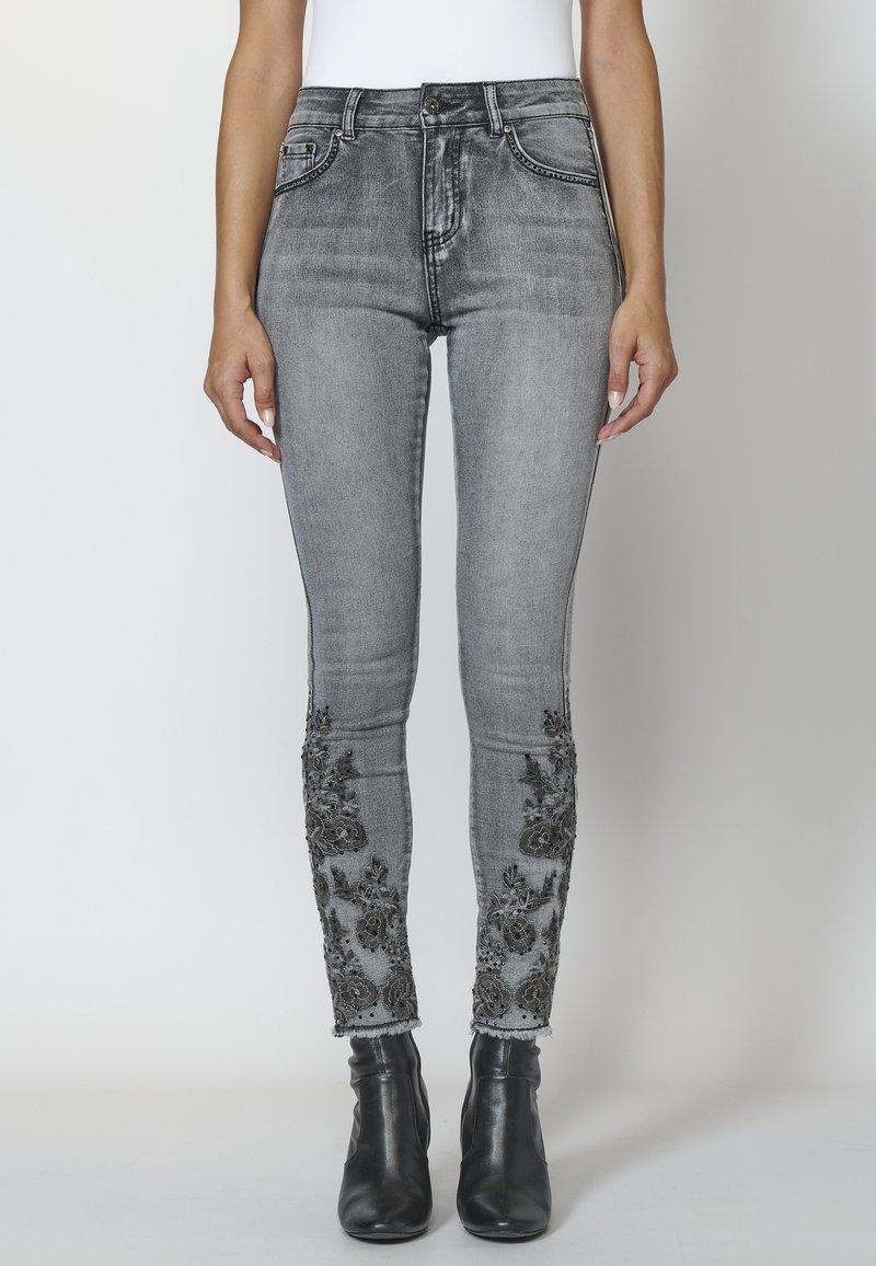 Šedé skinny džíny z denimu s dekorativními černými vyšívanými květinovými vzory na kotnících. Klasický pětikusový styl s přiléhavým siluetou.