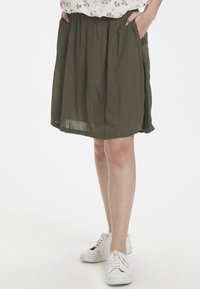 Olivenfarvet nederdel lavet af letvægtsstof, med en løs pasform, elastisk talje og to sidelommer. Båret med hvide sneakers.