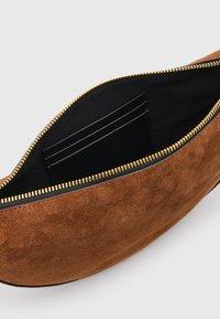 Ruskea mokka laukku kultaisella vetoketjulla. Sisäosa vuorattu mustalla, ja siinä on korttipaikkoja. Pyöristetty muoto, sileä pinta ja minimalistinen design.