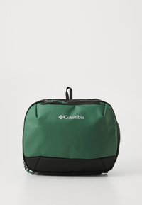 Bolso de tela en verde y negro de Columbia con forma rectangular, presenta un cierre superior con cremallera y un asa pequeña. Logotipo visible en la parte frontal.