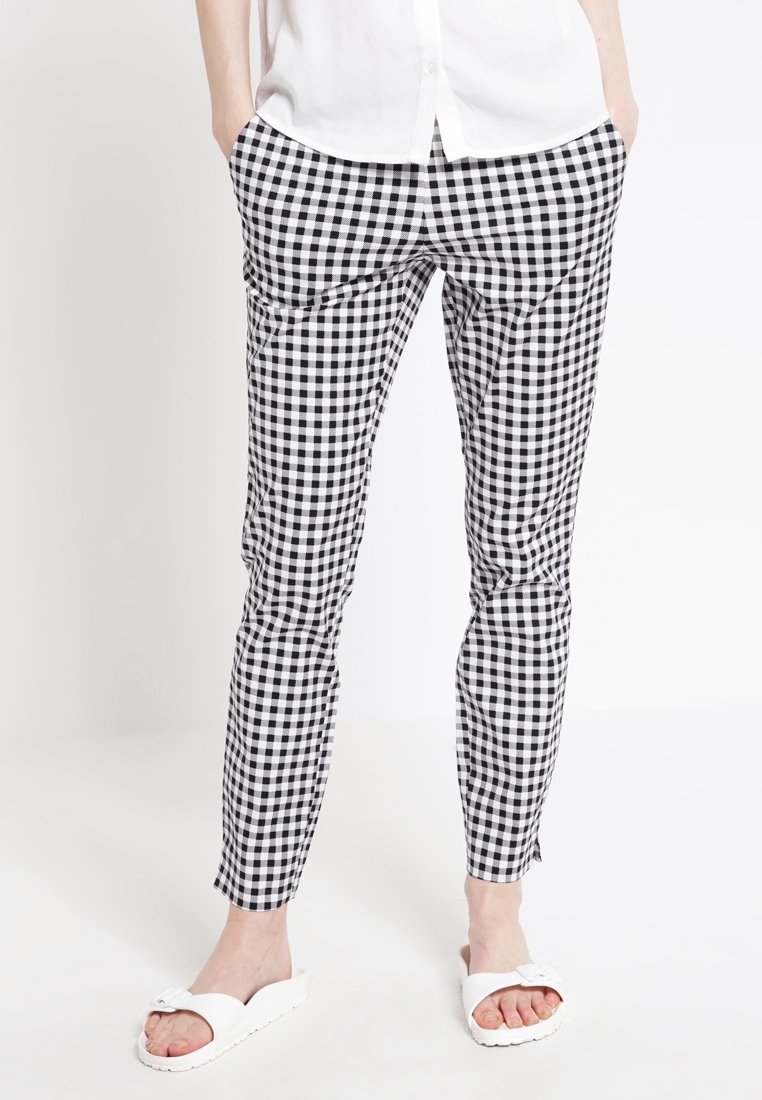 Un pantalon à carreaux noir et blanc présentant une coupe slim, un tissu lisse et deux poches latérales, associé à des sandales blanches à enfiler.
