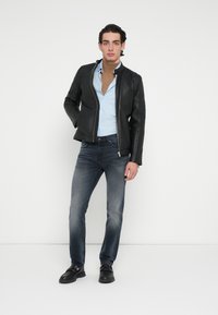 Geacă neagră de piele, cămașă bleu deschis, blugi gri și pantofi negri. Ținuta prezintă un design mulat și accente hardware minimale.