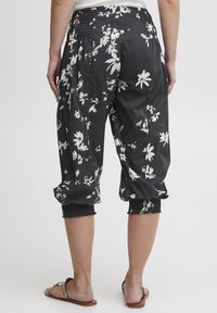 Czarne, krótkie spodnie w kwiaty wykonane z lekkiego, oddychającego materiału; mają marszczoną talię i ściągacze w nogawkach z białymi wzorami kwiatów.