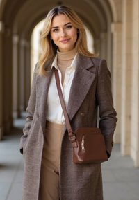 Borsa a tracolla in pelle marrone con zip e design a contrasto, abbinata a un cappotto grigio testurizzato doppiopetto e pantaloni beige.