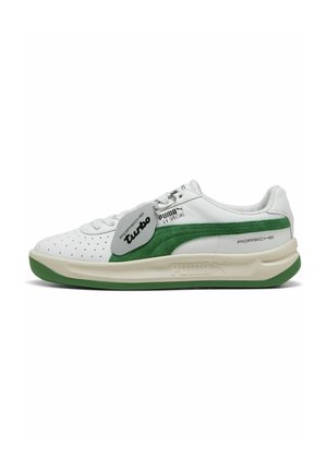 Baskets blanches avec des accents en suede vert, motif perforé, semelle en caoutchouc et étiquette métallique avec le label "Turbo". Marque PUMA sur le côté.