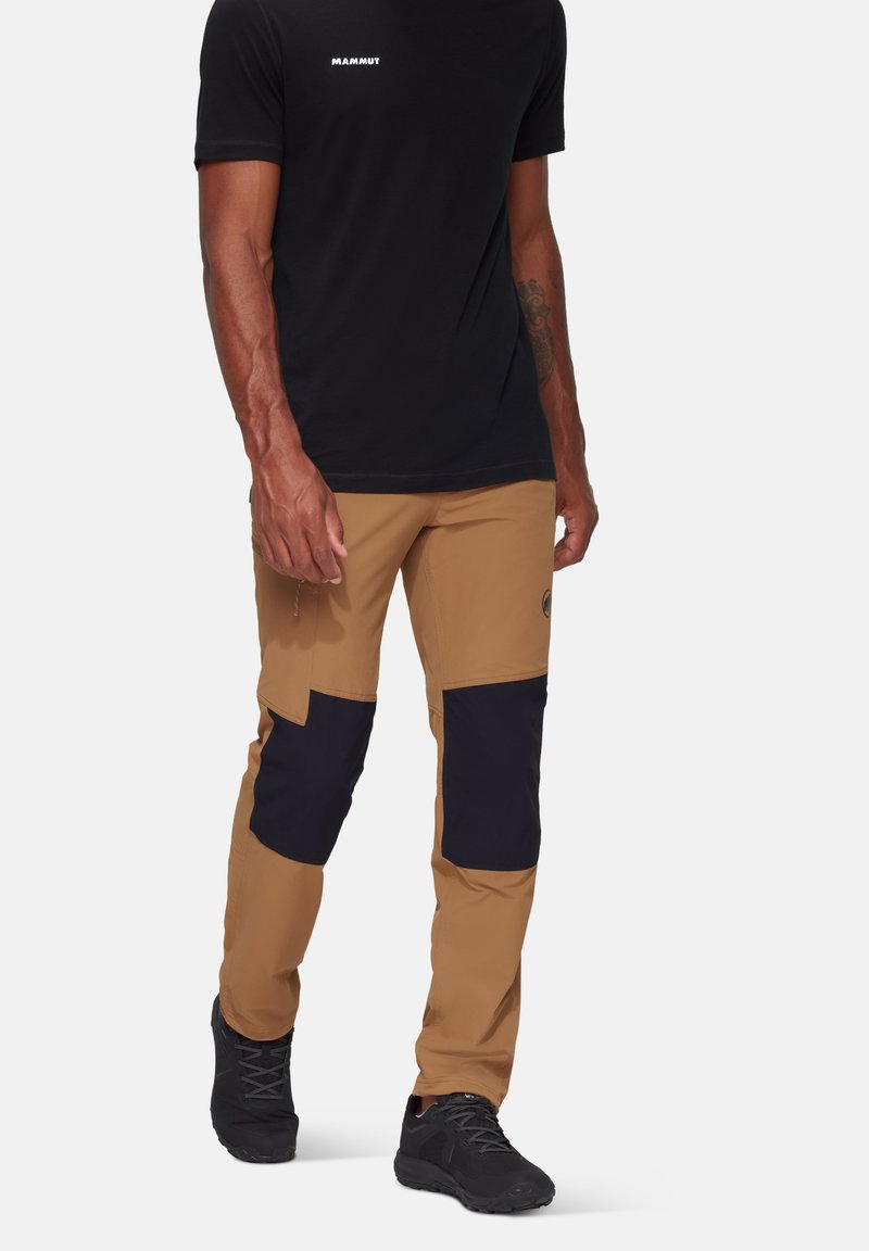 Bruine buitenbroeken met zwarte knieën, gemaakt van duurzaam materiaal. Voorzien van een slim fit ontwerp en versterkte stiksels voor extra stevigheid.