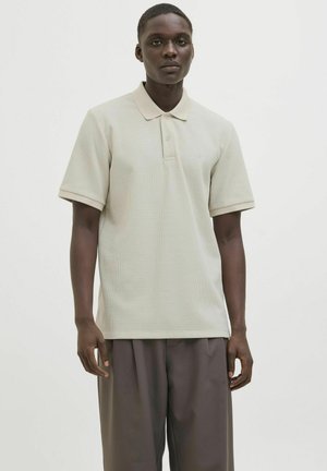Svijetlosmeđi polo majica izrađena od teksturirane tkanine, s klasičnim ovratnikom i kratkim rukavima. Majica ima slim fit kroj i suptilne detalje.