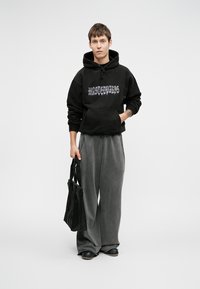 Hanorac negru cu grafică "WASTEDPARIS", asortat cu pantaloni largi gri. Include o geantă tote neagră, pe un fundal neutru.