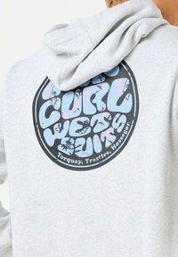 Sweat à capuche gris avec un grand graphique circulaire au dos, affichant le texte "CURL WETSUITS" en bleu et rose, avec des détails floraux.