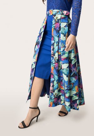 Maxikleid mit floralem Muster und tailliertem Bund in Blau und Grün, kombiniert mit einem einfarbigen blauen Kleid und schwarzen Absatzsandalen.